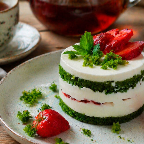 Готовое изумрудное пирожное с клубникой, украшенное свежей ягодой и мятой, крупным планом на белой тарелке