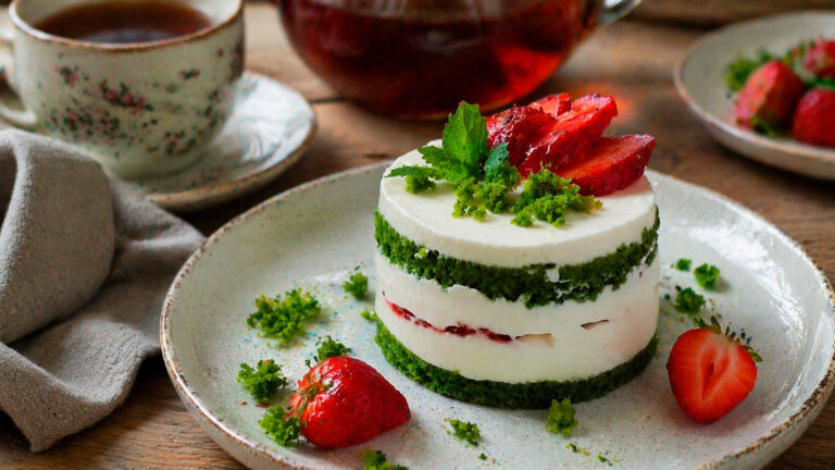 Готовое изумрудное пирожное с клубникой, украшенное свежей ягодой и мятой, крупным планом на белой тарелке