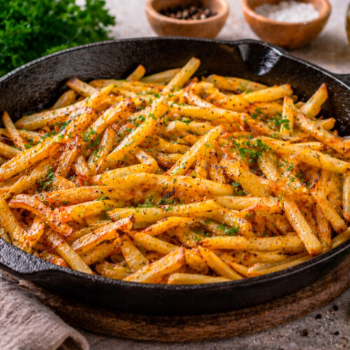 Тонкая хрустящая жареная картошка соломкой на чугунной сковороде, посыпанная паприкой и укропом