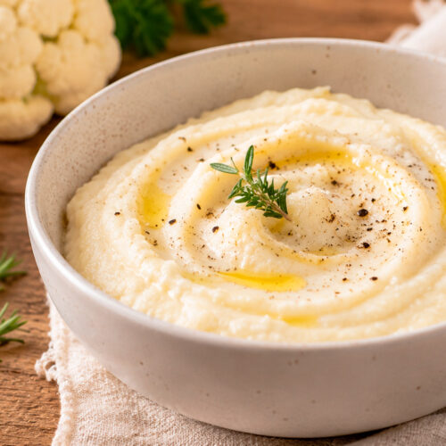 Воздушное пюре из цветной капусты на деревянном столе, рядом кусочек масла и веточка розмарина.